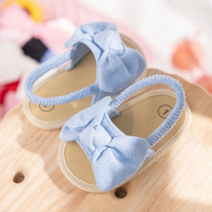 Light blue baby girl soft sole bow sandals resting on a natural wood surface.