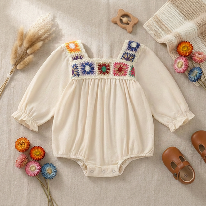 Flat lay view of the long-sleeve floral crochet baby bodysuit arranged with matching brown leather shoes, dried pampas grass, and colorful knit flowers.