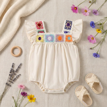 Flat lay arrangement featuring the crochet flower baby romper styled with small white sandals, a wooden teething ring, and decorative dried flowers.