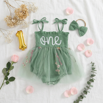 Aesthetic flat lay of the sage green "one" romper surrounded by rose petals, a gold "1" balloon, and eucalyptus—perfect for fairy one-derland inspiration.