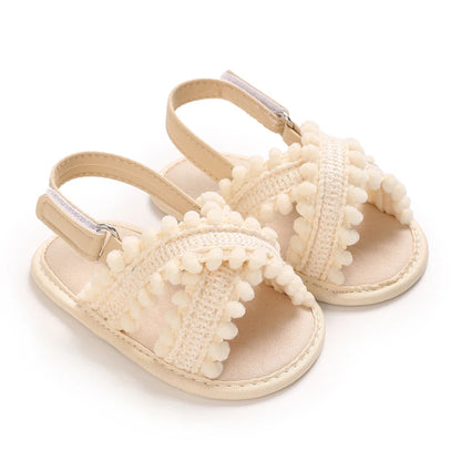 Cream boho infant girls pom pom sandals with cross-straps and non-slip soft sole.