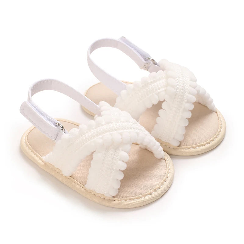 White first walker baby sandals with pom pom detail and flexible anti-slip sole.