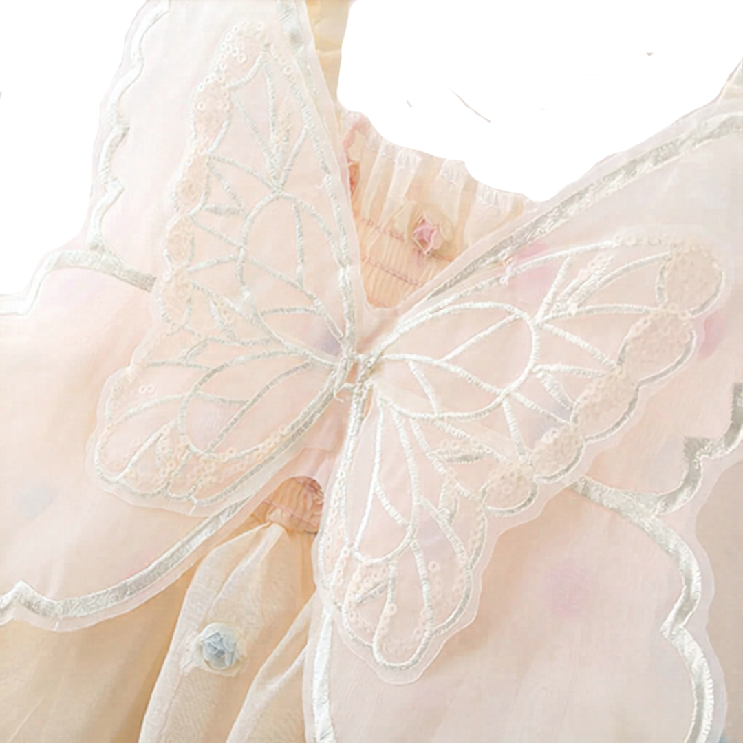Macromaterial detail shot of the sheer mesh butterfly wings on the back of the baby dress, showing white embroidery and sparkling sequin trim.