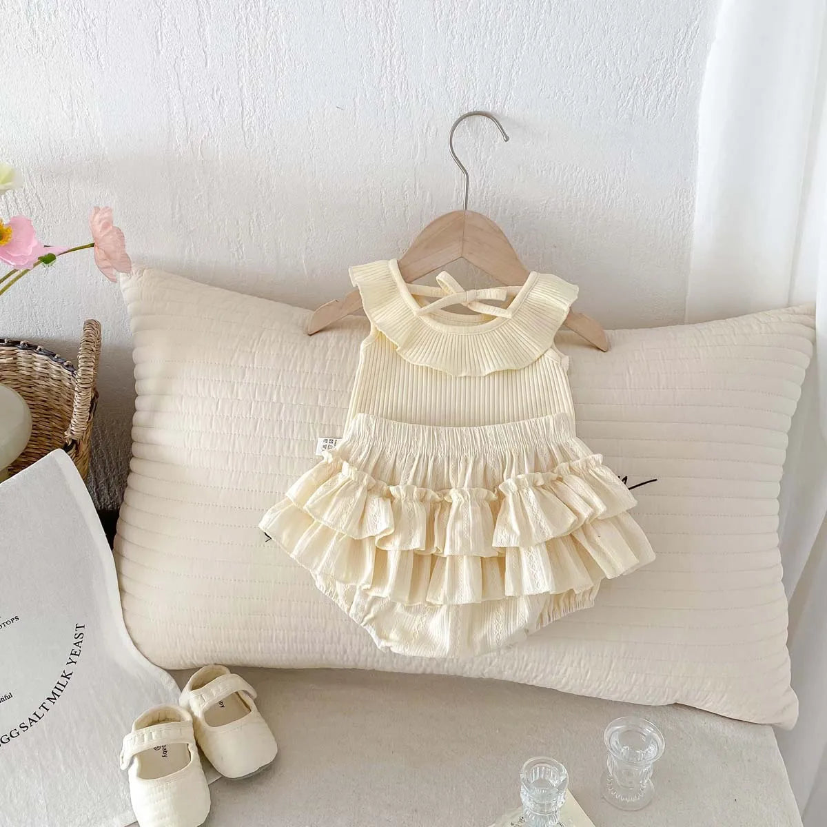 Boutique display of the cream 2-piece Aria set, highlighting the ruffled silhouette and premium fabric texture for infant girls from the back view.