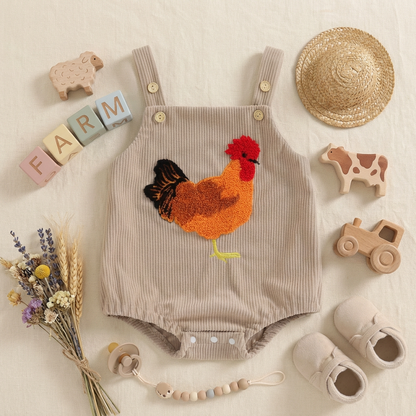 Children's romper with rooster design surrounded by toys and decorative farm items on a light background