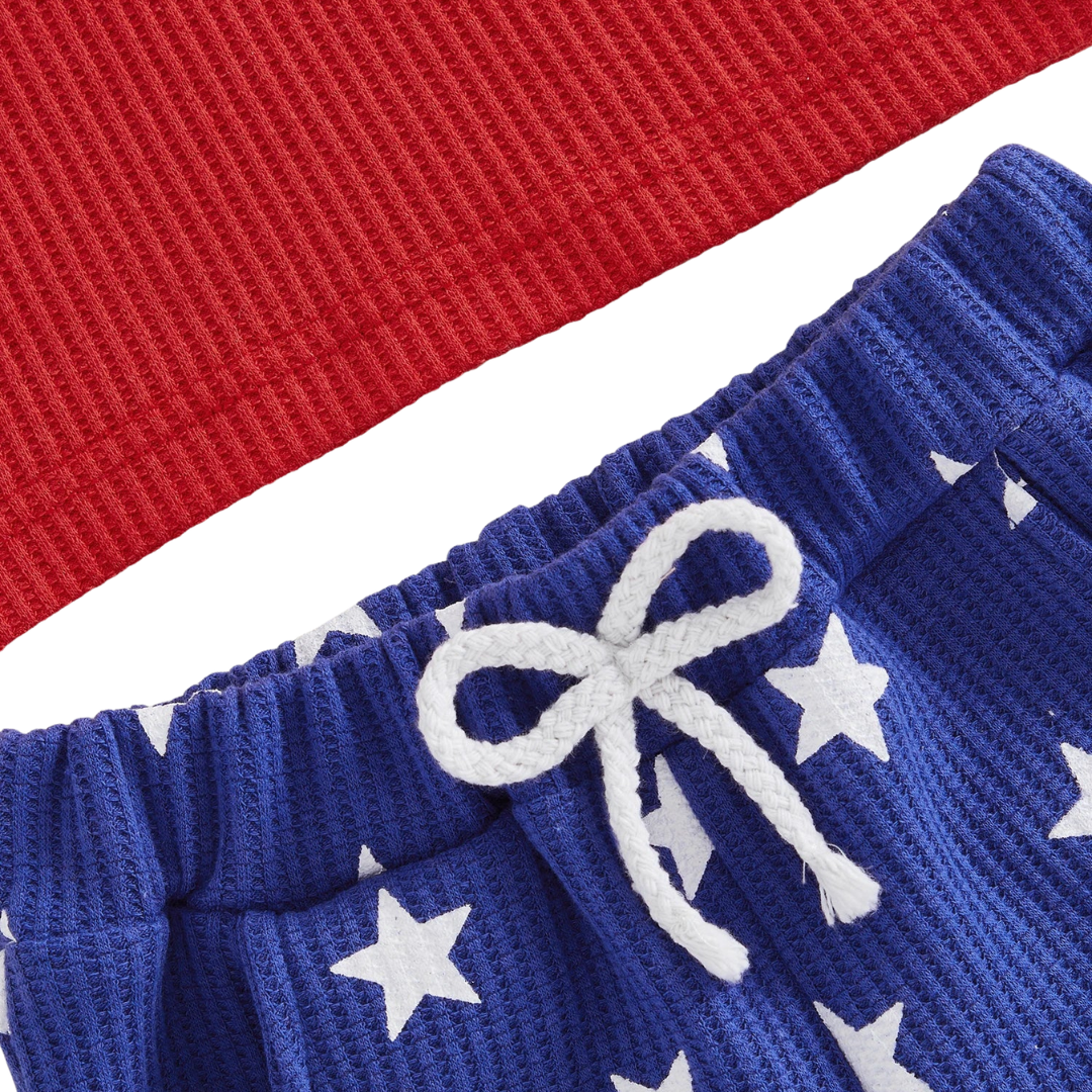 Close-up of the flexible elastic waistband and decorative white front tie on the toddler boys blue star-print shorts.