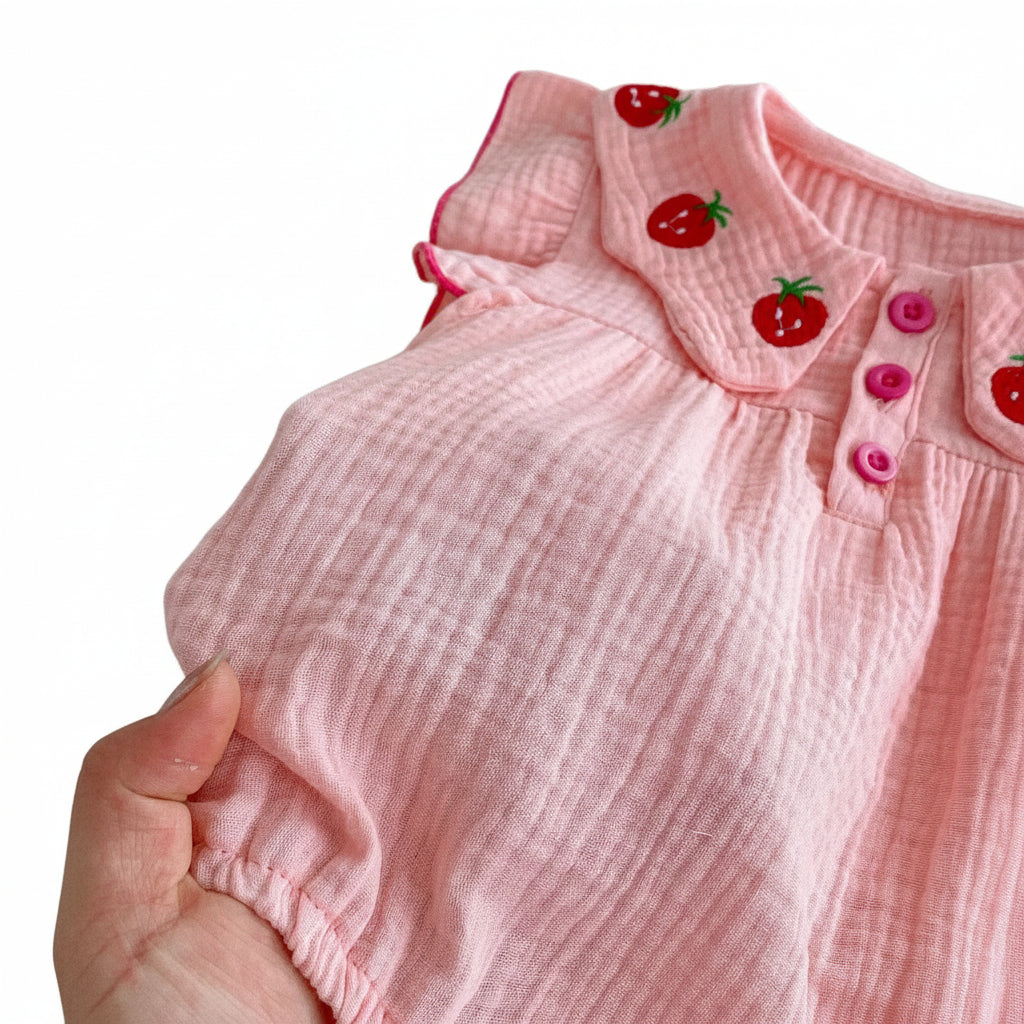 A close-up view of a hand holding the pink muslin cotton romper fabric to display its soft, breathable, and crinkled texture.