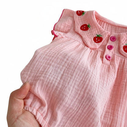 A close-up view of a hand holding the pink muslin cotton romper fabric to display its soft, breathable, and crinkled texture.
