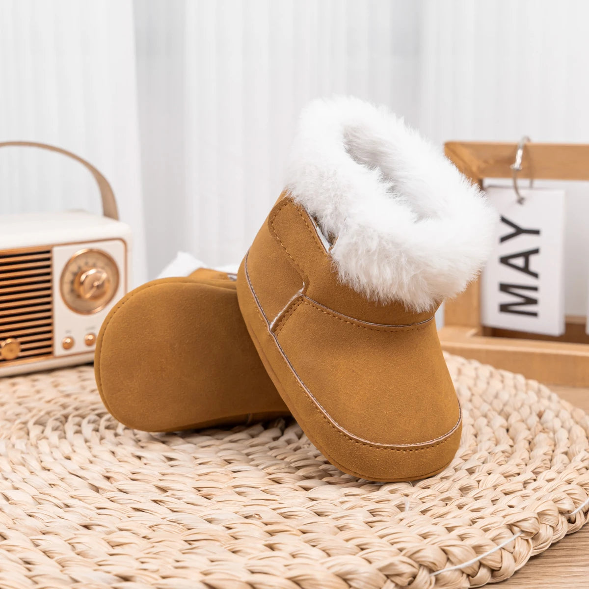 Brown baby soft sole crib boots displayed on a woven mat next to a small vintage radio.