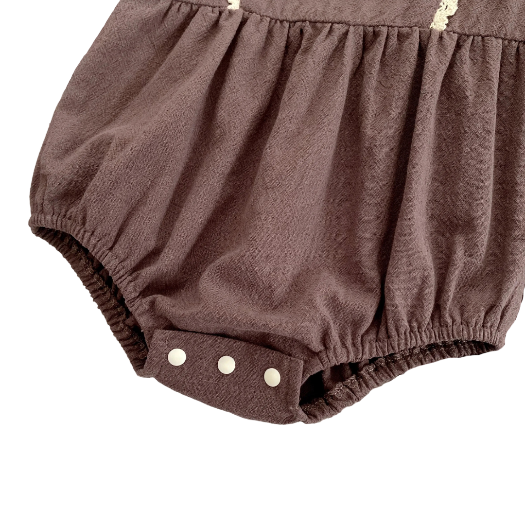 Close-up of the secure, fastened white bottom snap closures on the brown infant bubble romper.