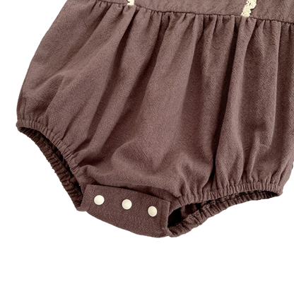 Close-up of the secure, fastened white bottom snap closures on the brown infant bubble romper.