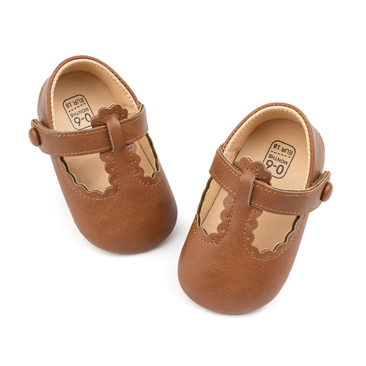 Top-down angled view of brown baby girl scalloped T-strap first walker shoes.