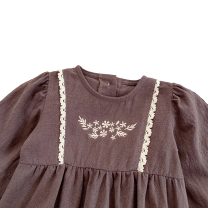 Close-up of the delicate white floral embroidery and vertical lace trim on the chest of the brown cotton baby girl bubble romper.