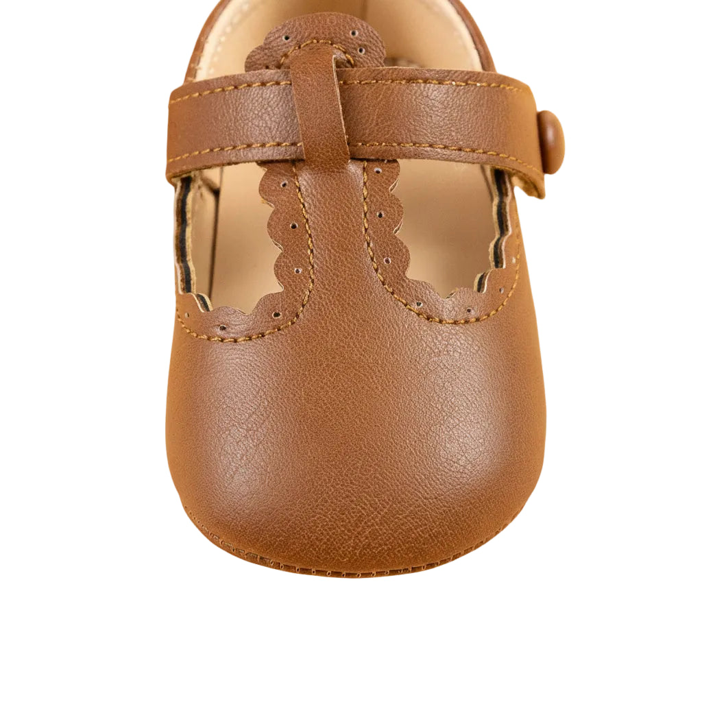 Close-up front view of a single brown baby girl T-strap shoe highlighting the scalloped toe detail.