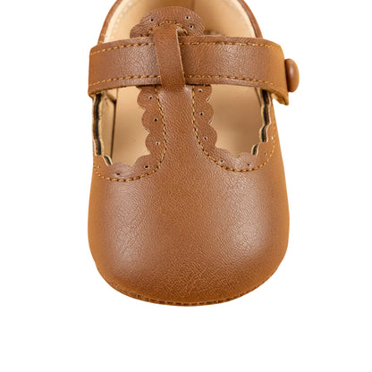 Close-up front view of a single brown baby girl T-strap shoe highlighting the scalloped toe detail.