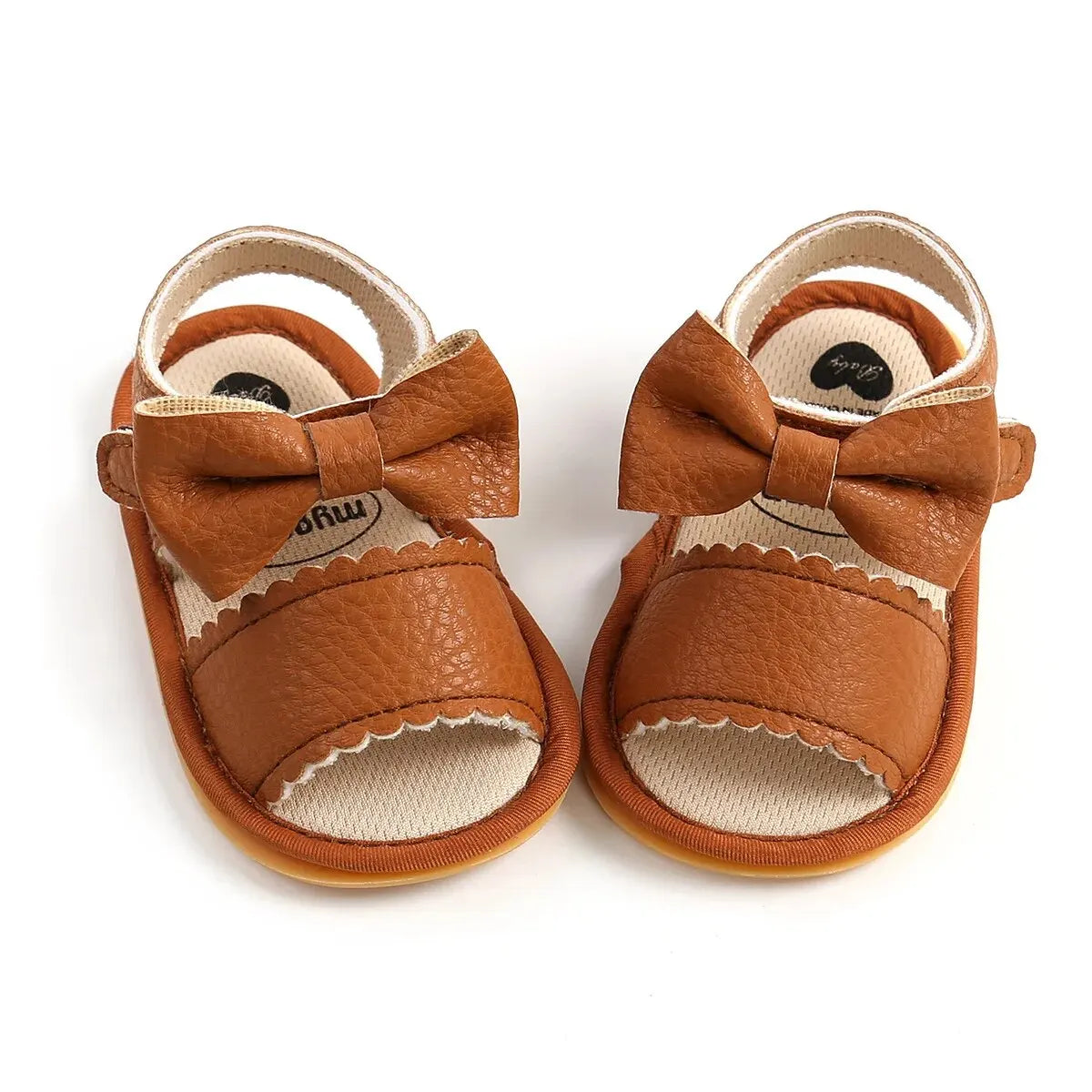 Pair of tan brown leather baby girl first walker sandals featuring a large textured bowknot and classic scalloped edges.