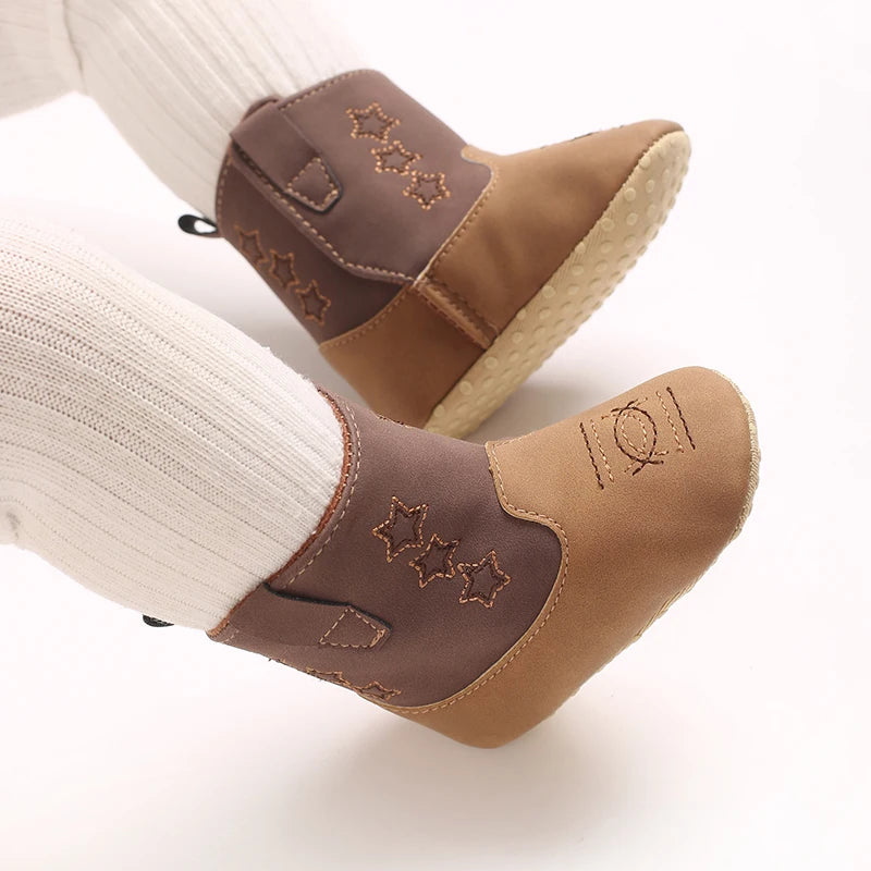 Top-down view of a baby wearing brown and tan soft sole western booties with white tights.