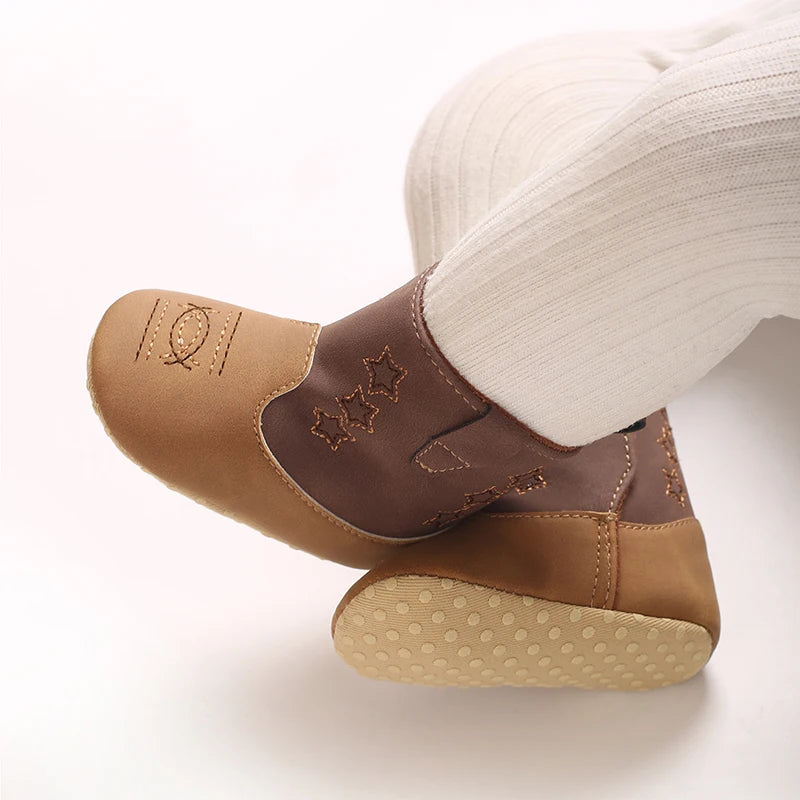 Close up of a baby wearing brown and tan cowboy boots, showing the flexible anti-slip dotted soft soles.