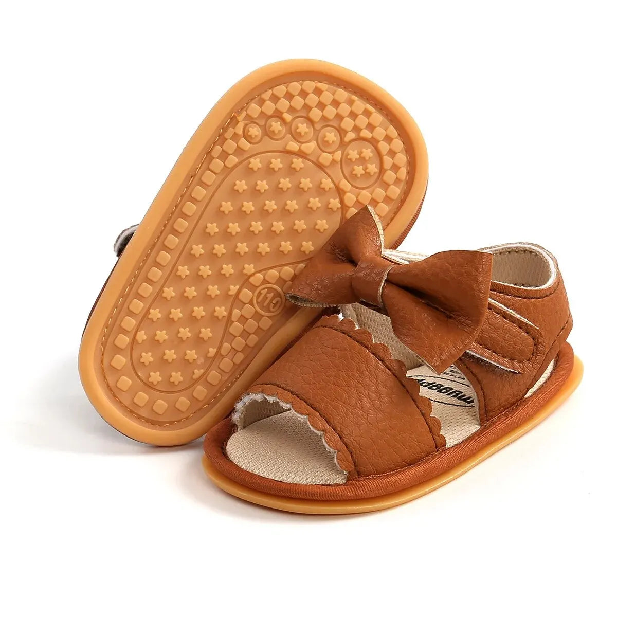 Pair of brown tan toddler girl sandals with one shoe flipped over to reveal the textured anti-slip rubber grip pattern on the bottom outsole.