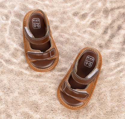 Overhead view of brown infant summer sandals resting on sand.