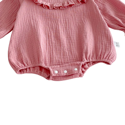 Detail shot of the bottom front of a pink cotton gauze baby bubble romper showing three white snap buttons securely closed.