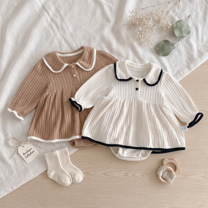 Flat lay of chestnut and ivory baby girl cable knit romper dresses on a textured blanket with baby socks.