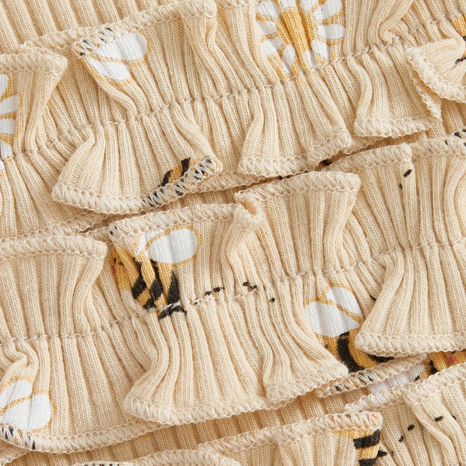 Close-up of the beige ribbed cotton blend fabric showing the bumblebee and daisy pattern and sweet ruffle butt detailing.