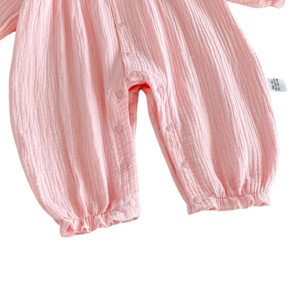 Close-up of the securely fastened bottom inseam snaps and elastic leg cuffs on the pink muslin baby jumpsuit.
