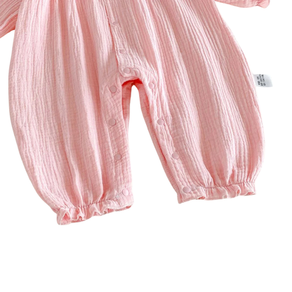 Close-up of the securely fastened bottom inseam snaps and elastic leg cuffs on the pink muslin baby jumpsuit.