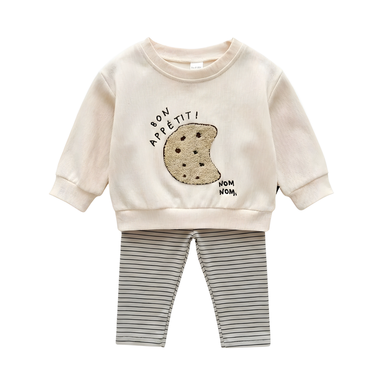 A two-piece baby outfit on a white background, featuring a cream ribbed long-sleeve pullover with a boucle cookie embroidery and "bon appétit!" text, paired with horizontal striped leggings.