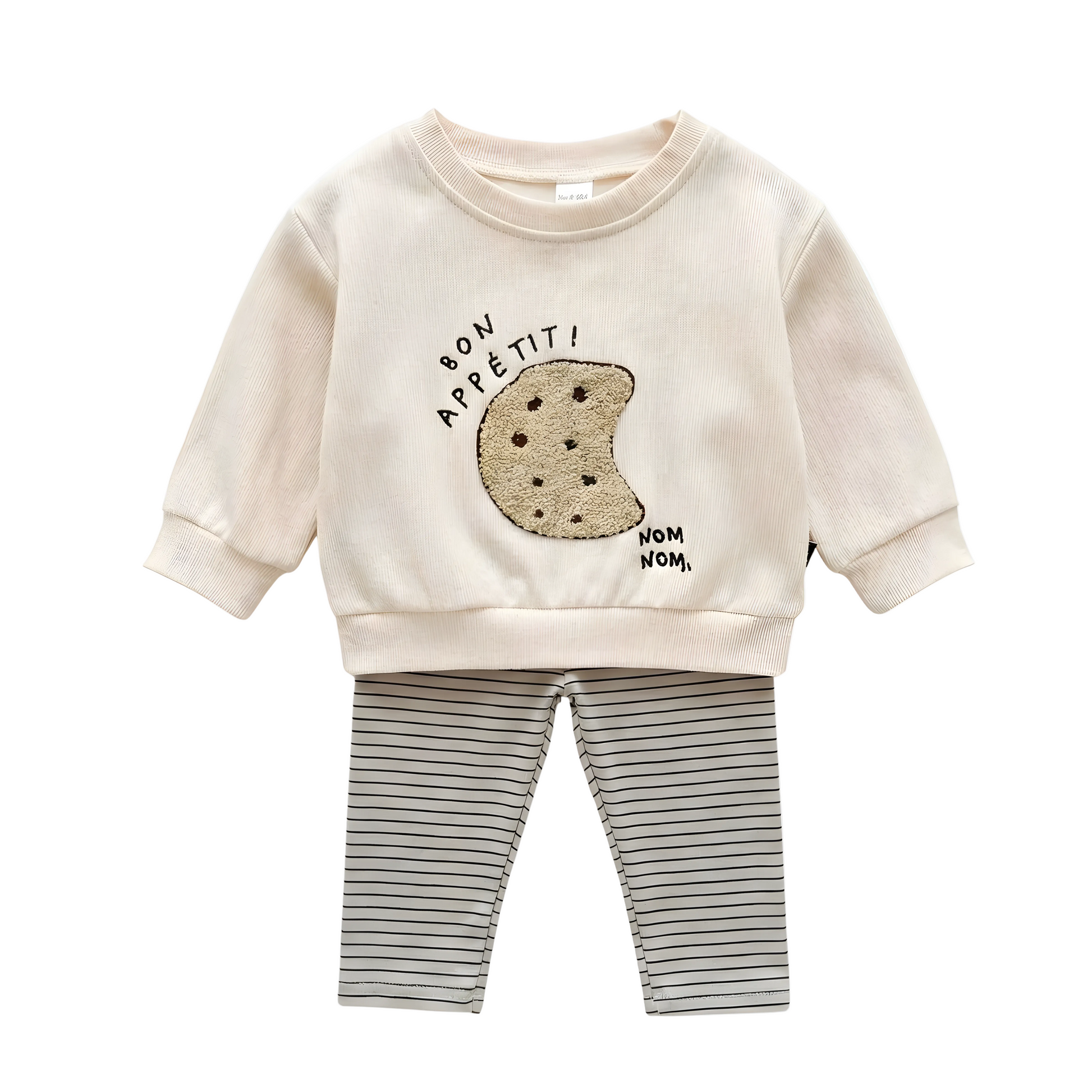 A two-piece baby outfit on a white background, featuring a cream ribbed long-sleeve pullover with a boucle cookie embroidery and "bon appétit!" text, paired with horizontal striped leggings.