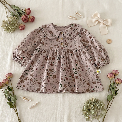 Styled flat lay of the Kidsely floral baby dress resting on a textured cream surface, surrounded by delicate dried flowers and a hair bow.
