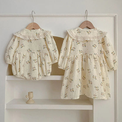 Back view of matching floral baby bubble romper and girls dress hanging on wooden hangers for sister matching outfit display.