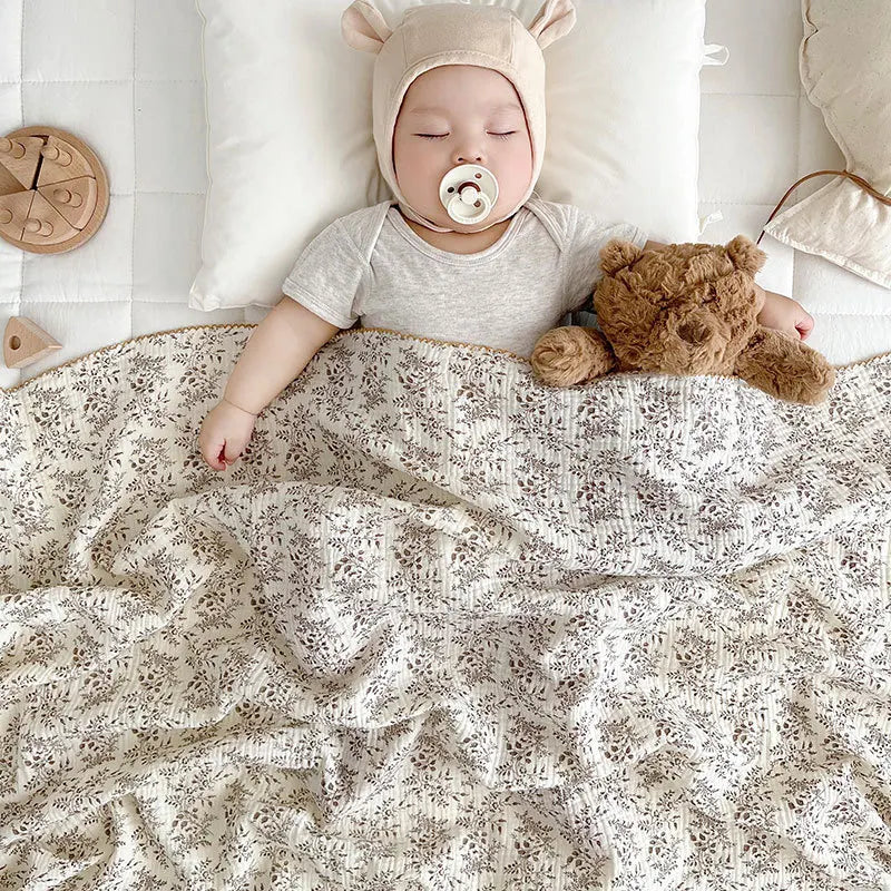 Close up of a baby with a pacifier sleeping peacefully under a breathable 2-layer taupe botanical summer gauze blanket.