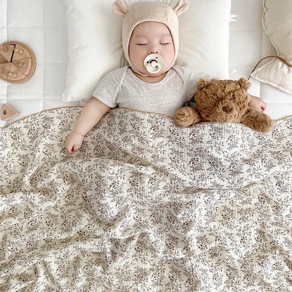 Close up of a baby with a pacifier sleeping peacefully under a breathable 2-layer taupe botanical summer gauze blanket.