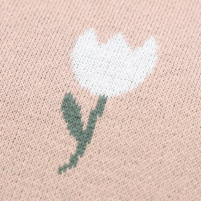 Detailed close-up of a white woven tulip flower design on the soft blush pink cotton knit nursery blanket fabric.