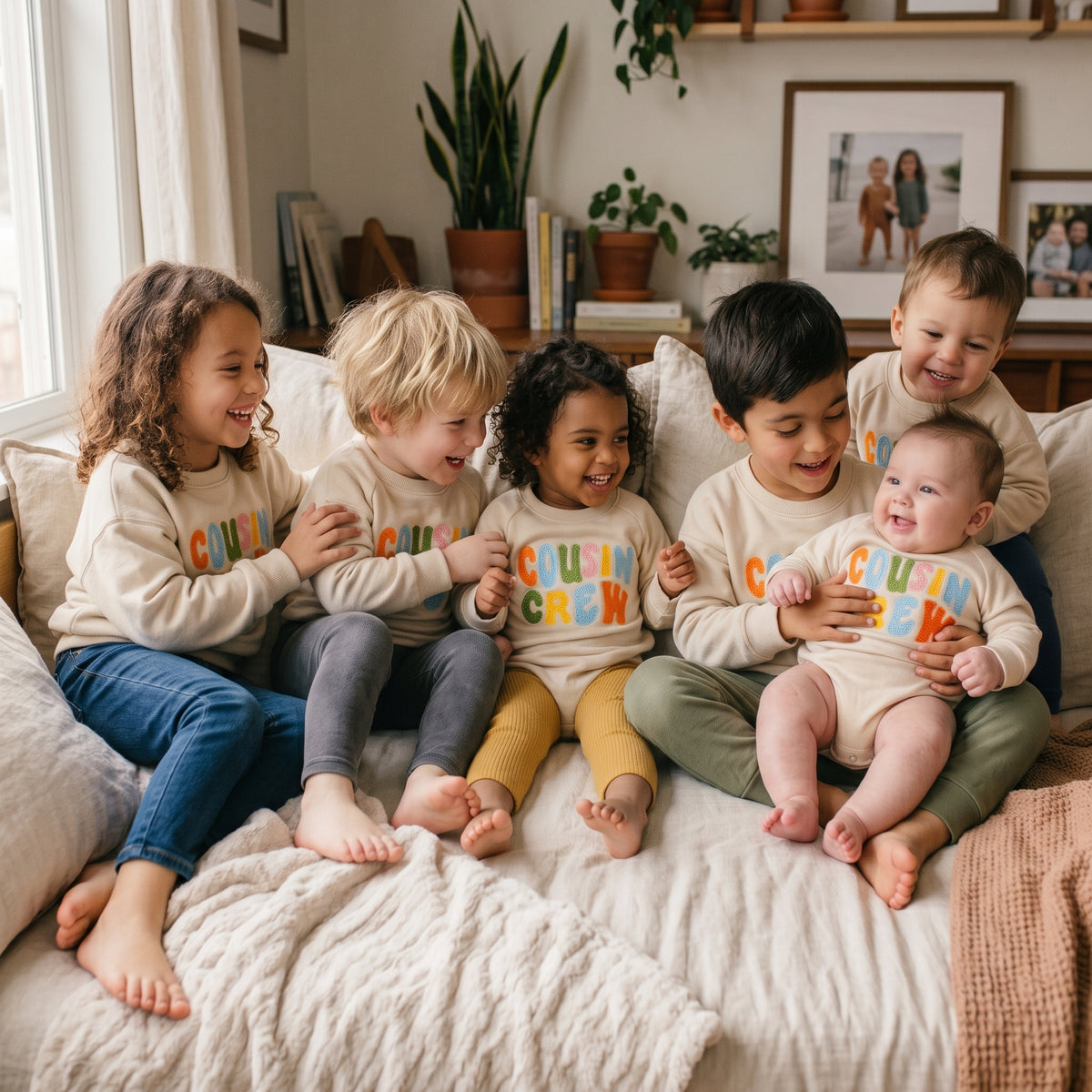 Group of cousins sitting together on a bed wearing matching Cousin Crew neutral outfits for a family photoshoot