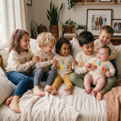 Group of cousins sitting together on a bed wearing matching Cousin Crew neutral outfits for a family photoshoot