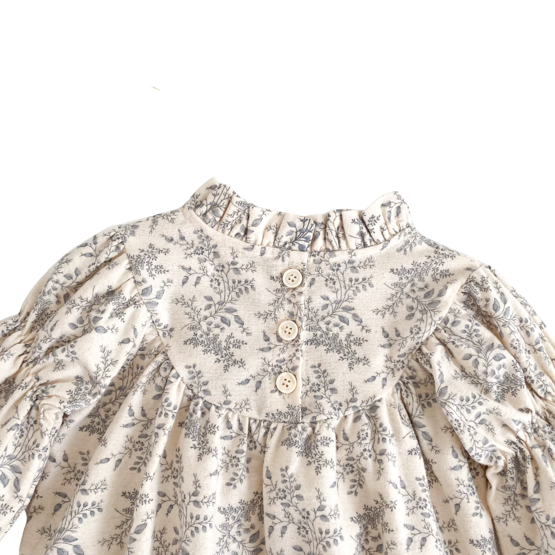 Close-up of the upper back of the cream and gray floral baby romper showing the single button closure and ruffle collar.