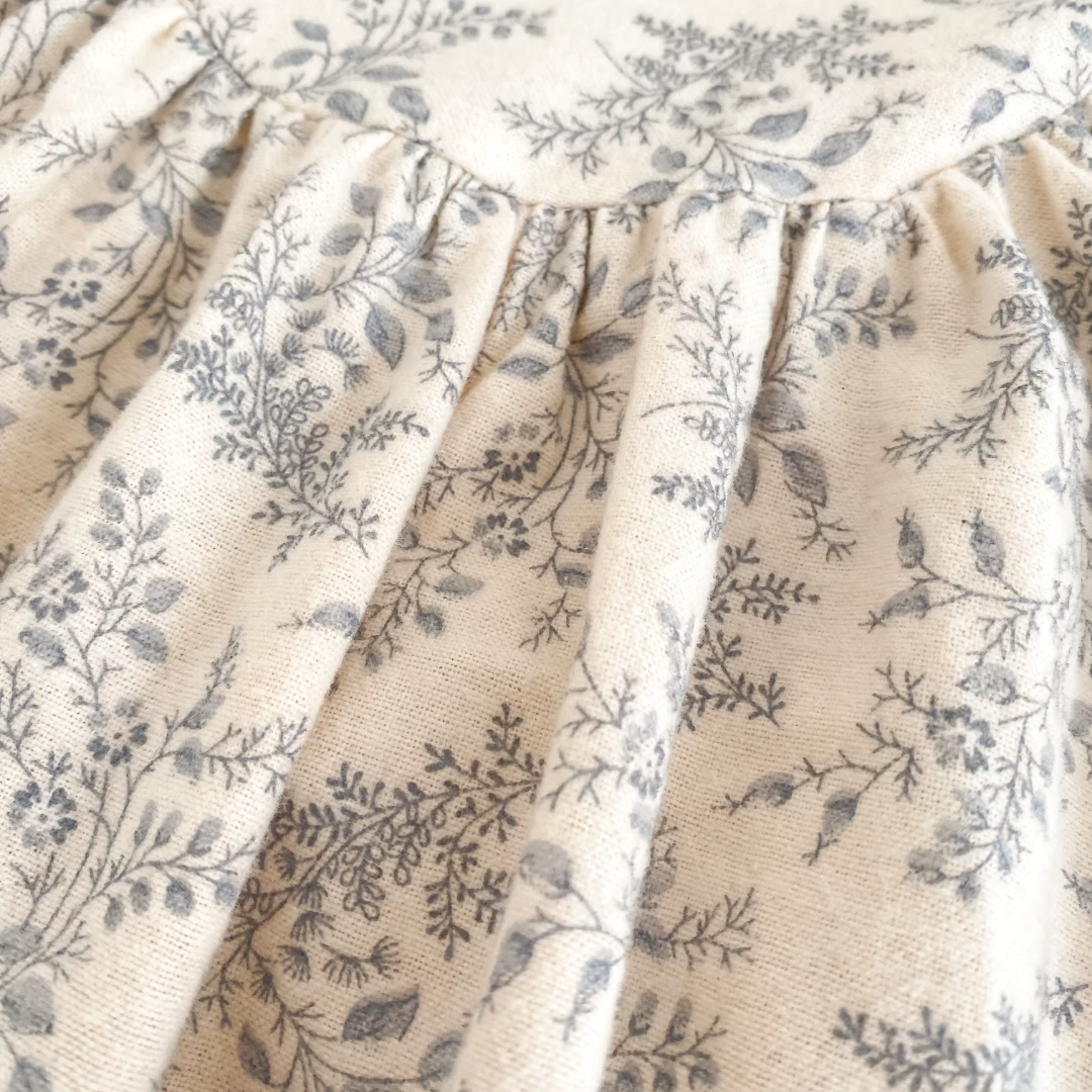 Close-up of the cream and gray botanical floral fabric pattern and shoulder seam on the baby romper.