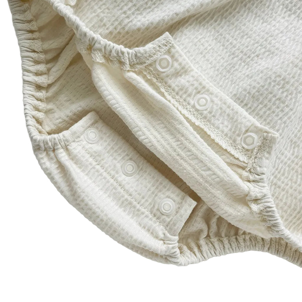 Inner view of the high-quality open metal snap closures on the cream baby girl bodysuit.