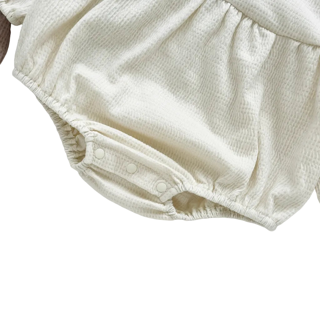 Close-up of the soft elastic gathered leg opening on the cream off-white infant bubble romper.