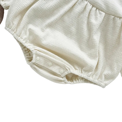 Close-up of the soft elastic gathered leg opening on the cream off-white infant bubble romper.