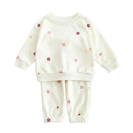 Full flat lay photo of a boutique off-white two-piece baby outfit, including a sweatshirt and joggers, decorated with small, multi-colored embroidered flowers on a white background.
