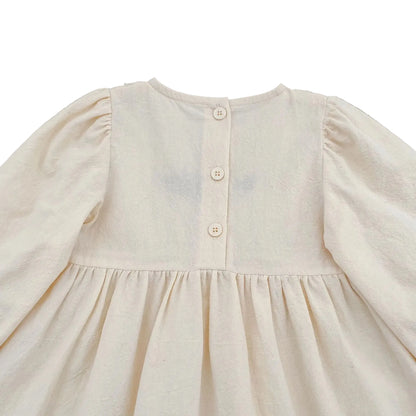 Close-up of the upper back section of the cream baby girl romper showing the three button closures.