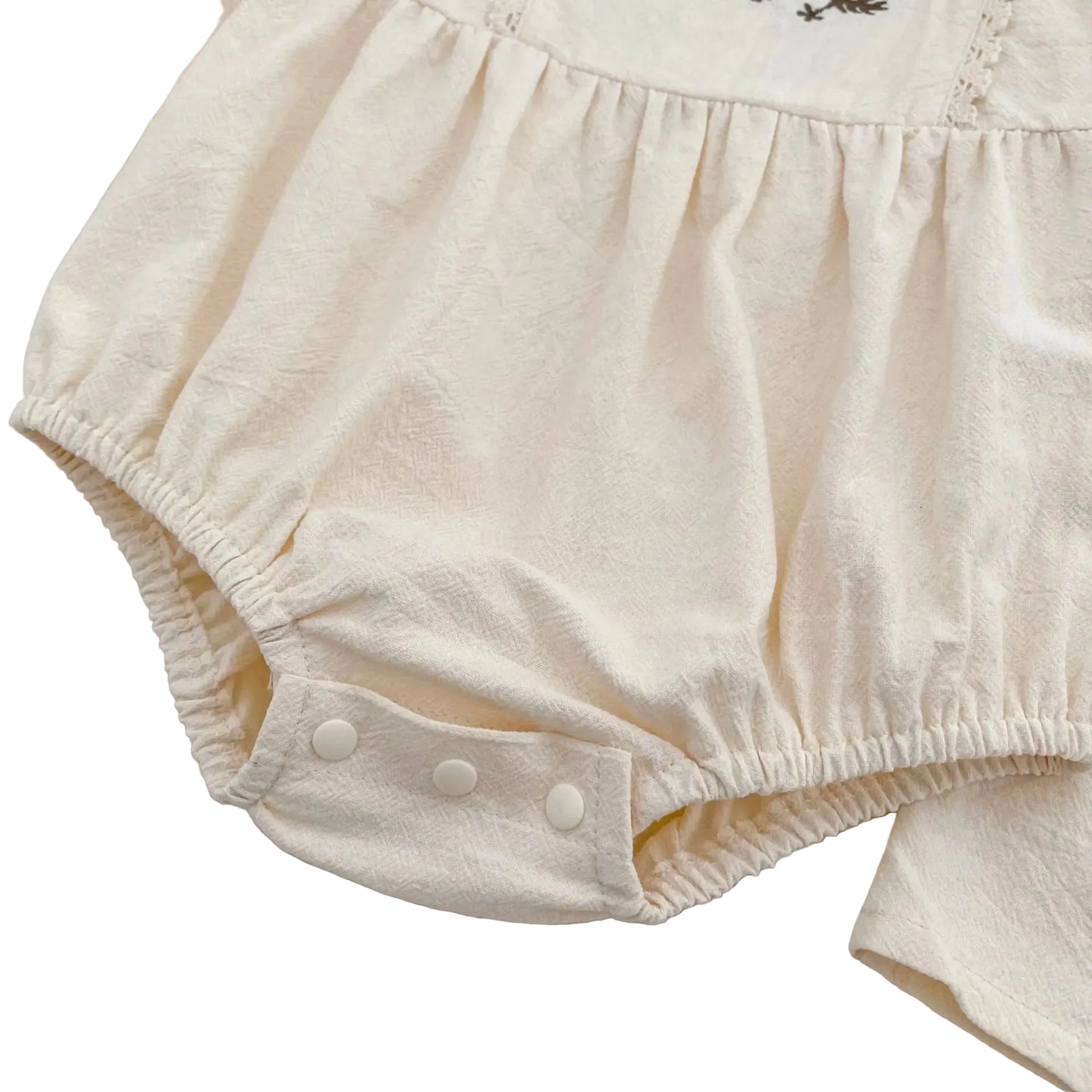 Close-up of the secure, fastened white bottom snap closures and gathered elastic on the cream infant bubble romper.