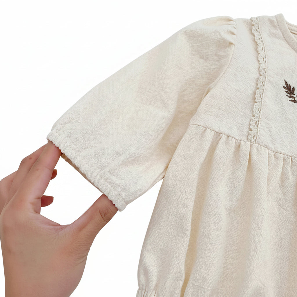 A hand holding the sleeve of the cream infant bubble romper, showcasing the comfortable elastic wrist cuff.