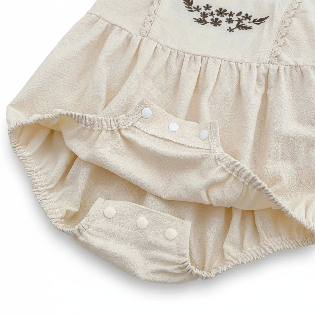Close-up showing the unfastened bottom snap closures on the cream cotton bubble romper for easy diaper changes.