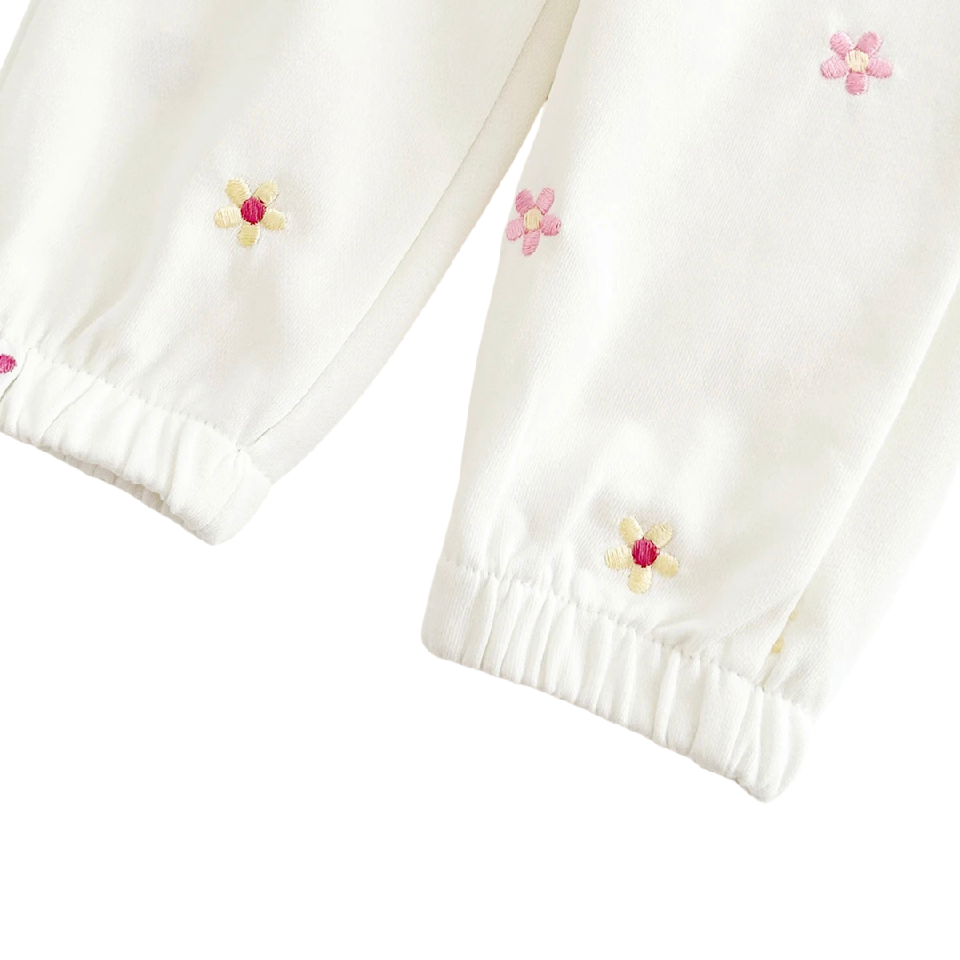 Detail shot focused on the ribbed ankle cuffs of the off-white baby joggers, showing the gathered fabric and floral embroidery.
