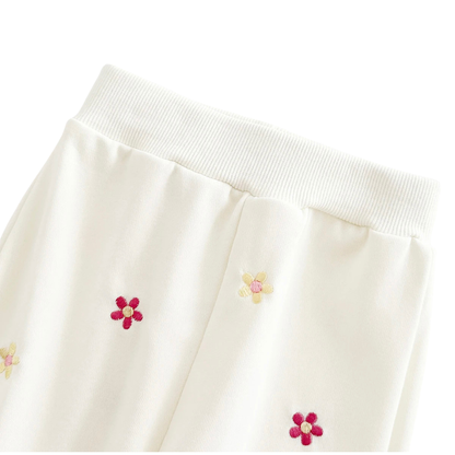 Close-up of the ribbed elastic waistband of the off-white baby pants, displaying the fabric quality and the matching floral embroidery.